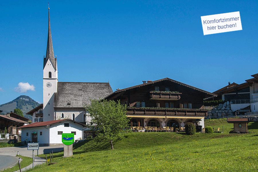 Im Vordergrund eine grüne Wiese, im Hintergrund die Terasse des Cafe and links die Kirche von Schwendt